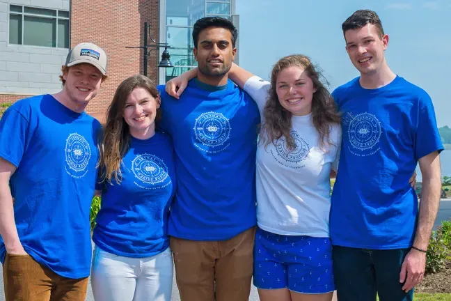 Five U N E students wearing matching blue U N E t-shirts pose happily